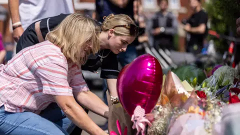 PA Media People lay flowers near the scene in Hart Street, Southport, where three children died and eight were injured in a "ferocious" knife attack during a Taylor Swift event at a dance school on Monday.