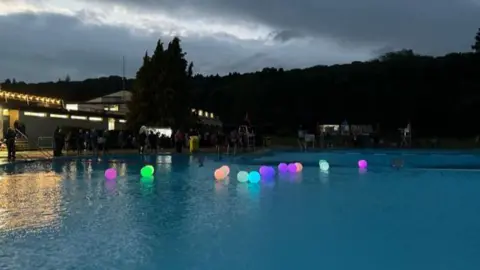 Julia Bryson/BBC Light -up multicoloured inflatable balls on the lido water at dusk