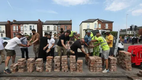 Reuters / Temilade Adelaja Volunteers rebuild the fence outside Southport Islamic Society Mosque, after a violent protest, following a vigil for victims of the knife attack