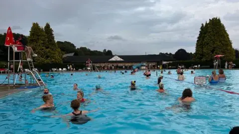 IPLCG Swimmers in the outdoor pool watched over by a lifeguard sitting in a raised seat