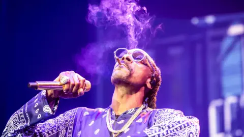 EPA Snoop Dogg smokes while holding a microphone and performing on stage