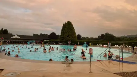 Julia Bryson/BBC Hundreds of swimmers in the outdoor pool at dusk