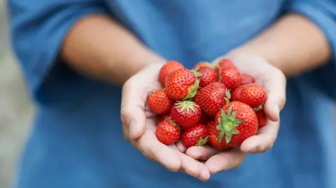 Getty Images A woman holding a portion of strawberries with both hands.