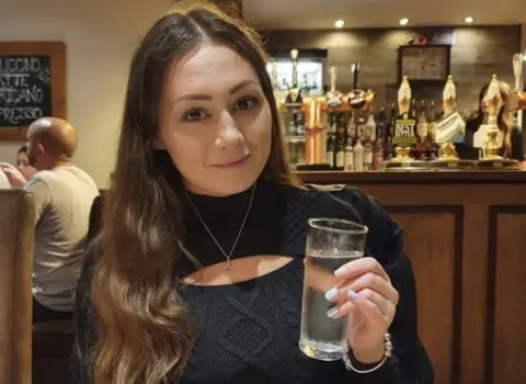 Belle is seen in a pub drinking water