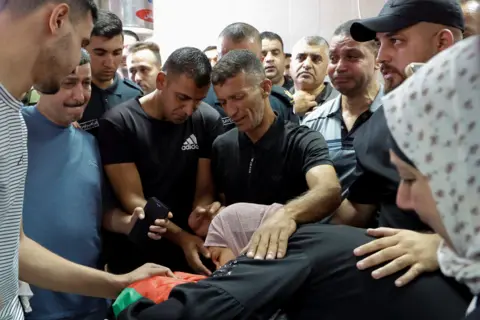 Reuters A woman lies on a corpse while others gather round at a funeral