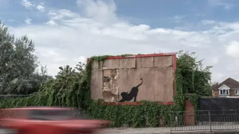 PA Media A black silhouette of a stretching cat painted on a dilapidated empty brown billboard