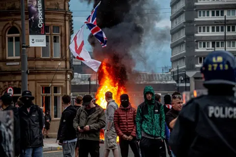 Getty Images Anti-immigration protesters gather in front of a burning Citizens Advice bureau 