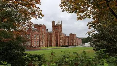 PA Media A general view of the main building of Queen's university - a red brick grand building. There are leafy green trees in the foreground