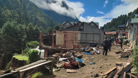 Khumbu Pashanlhamu Rural Municipality People walk down a dirt road amid rubble and destroyed buildings beside a partially collapsed hillside