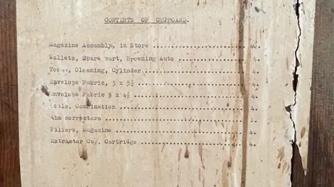 Clare Mulley Typed list of weapons and equipment and corresponding numbers of amounts on torn sheet of paper on a wooden background