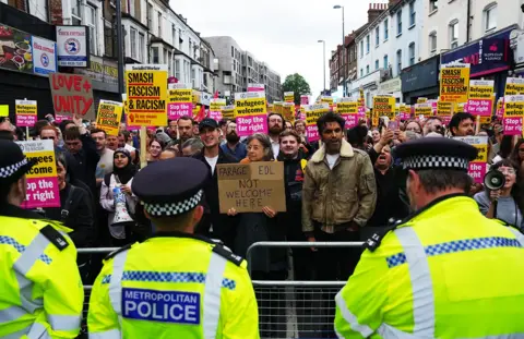 Getty Images Police officers line up in front of a mass of anti-racism protesters holding placards on Hoe Street in Walthamstow on 7 August