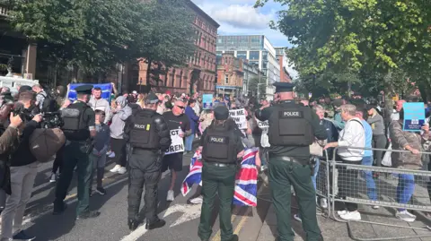 Police officers facing away from the camera and towards a group of people holding signs and union flags