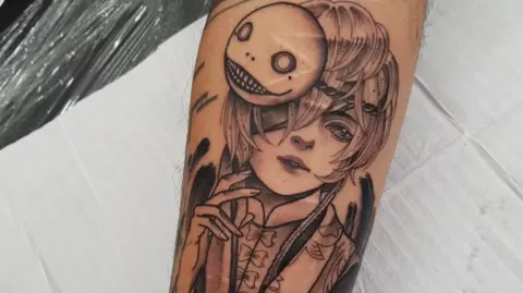 Löiz Dominguez A close up picture of a tattoo in black ink depicting an anime character. There are self-inflicted scars visible underneath the design 