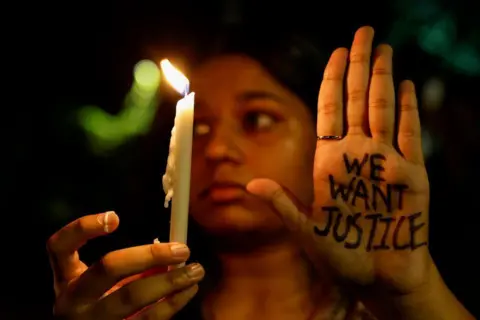 Reuters A woman holds a candle during a vigil condemning the rape and murder of a trainee medic at a government-run hospital in Kolkata, on a street in Mumbai, India, August 14, 2024