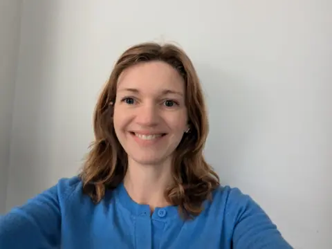 Anna Kenyon A smiling Anna Kenyon in a blue top in front of a white wall