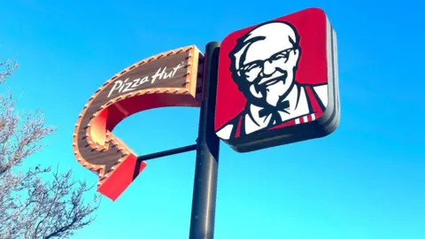 Getty Images Sign with an arrow for Pizza Hut on the left and the KFC Colonel logo on the right