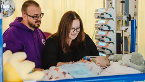  Jones family/PA Wire Stuart Jones in a purple hoodie and Laura Osborne in a black top sit by William in an incubator