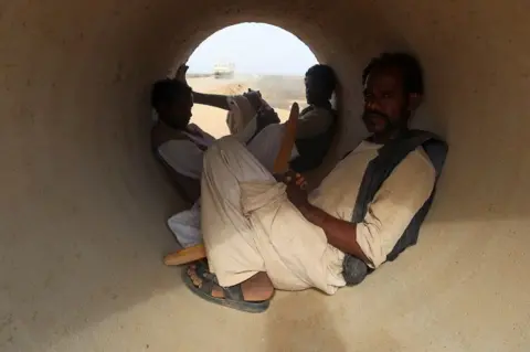 EL TAYEB SIDDIG / REUTERS Three people shelter from the sun inside a cement pipe.