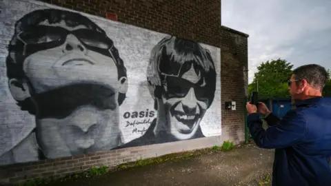 Getty Images Oasis fan photographing a new mural of Liam and Noel Gallagher of Oasis, created by Manchester street artist Pic.One.Art., on the side of the Sifters Record store in Burnage, in Manchester