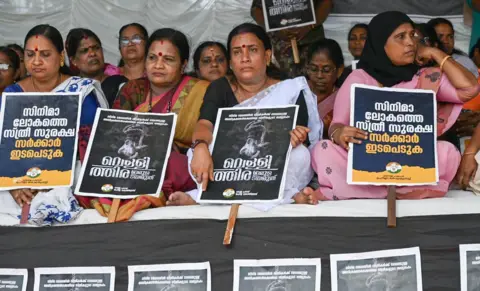 Arun Chandra Bose/BBC Women from the Mahila Congress sit in protest, holding up posters,  demanding action on Hema panel report in Kochi on Friday