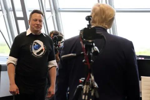 Reuters Musk facing the camera as we see the back of Donald Trump