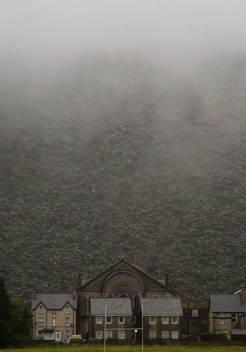 Jon Pountney A chapel and a collection of houses with a huge slate mountain behind them