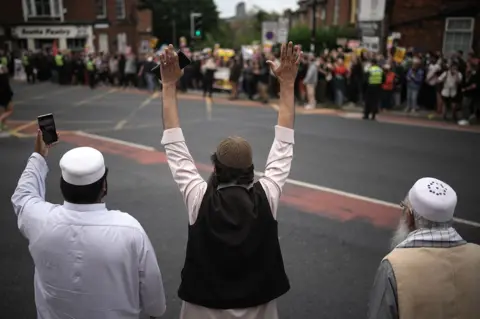 Getty Images Three Muslum men gesture towards a crowd of anti-racism protesters in Sheffield on 7 August