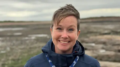 Anna Snow stands on a beach smiling at the camera