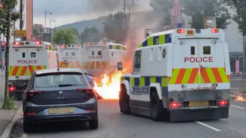 PA Media Vehicle on fire with several PSNI riot landrovers surrounding it