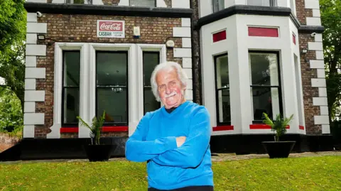 PA Original Beatles drummer Pete Best, 82, stood outside The Casbah Coffee Club building wearing a blue jumper with folded arms