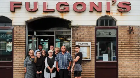 @mwktar The Fulgoni family, nine people of multi-generations stand in the entrance of their cafe