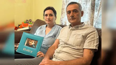 BBC Lindita Alushi and Kastriot Klosi sit on a sofa holding a photo of Daniel