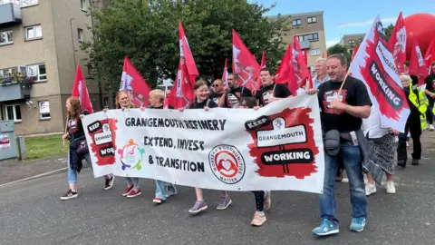 BBC People marching with a large rectangular banner, reading 'Grangemouth refinery extend, invest and transition' 