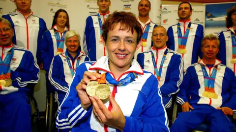 PA Media Wheelchair athlete Tanni Grey-Thompson pictured in 2004 with her two gold medals around her neck and with team members in the background.