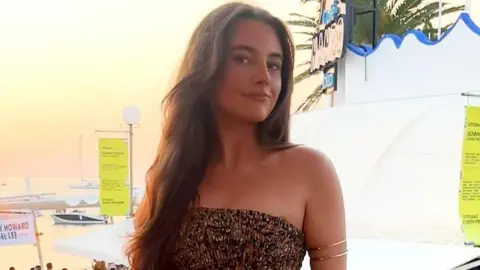 Instagram Emma Ramsay - young woman with long brown hair, wearing a brown dress and looking into the camera