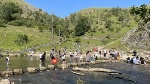 BBC Groups of people crossing a river using stepping stones