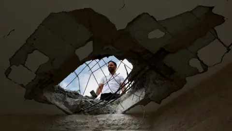 Reuters A man surveys damage to a building in Israel following a Hezbollah rocket and drone attack (25 August 2024)