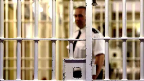 Getty Images A prison officer stands behind bars in a jail