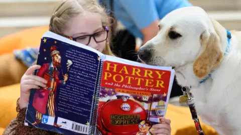 PA Media Anya, aged eight, reads Harry Potter and the Philosopher's Stone to Labrador-golden retriever cross Moxy at a special reading session hosted by Guide Dogs