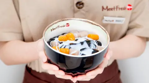 Getty Images A bowl of colourful dessert being held by a Meet Fresh employee in a beige top and brown apron