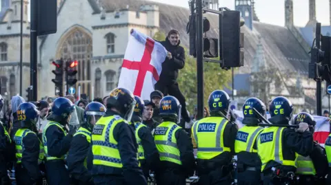 PA Media Row of policer officers in riot gear and counter protester with England flag