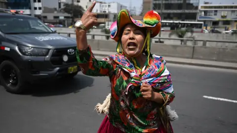 Getty Images An indigenous woman wearing a colourful hat and clothing raises her index finger and shouts against the former president Fujimori. A Toyota vehicle is pictured in the background