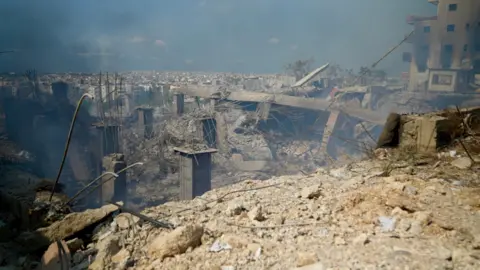 Goktay Koraltan / BBC Smoke rises from the ruins of what appears to be a factory in Beirut, Lebanon