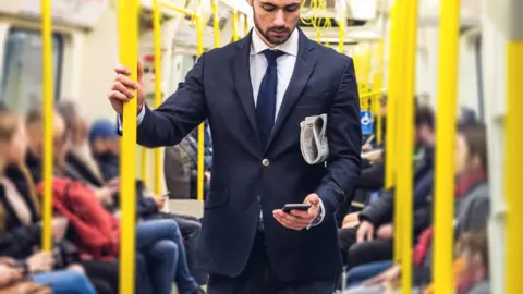 Getty Images Man in suit standing on Tube train with phone in hand and newspaper under his arm