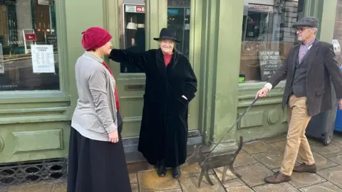 Charlotte Payn/The Maltings (Berwick) Trust Three people standing in the doorway. The woman to the left is wearing a red hat, the woman in the centre has a black hat and the man on the end has a grey cap. 