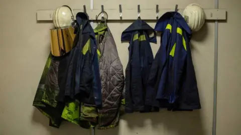 Jon Poutney Steelworkers' overalls and helmets are hung on a short row of coat hooks at the Port Talbot site.