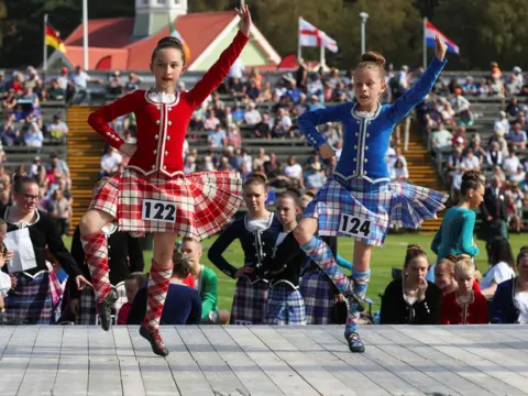 Reuters Girls dancing in traditional outfits, one red and one blue, with spectators behind them 