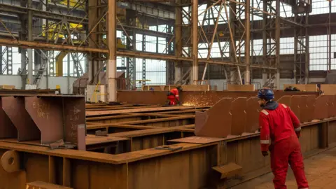 Getty Images A worker grinds pieces of steel during the construction of a barge at the production facility in Harland & Wolff Group Holdings shipyard in Belfast.