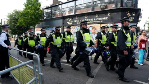 PA Media A group of police officers walk through the streets of Ladbroke Grove. They are holding blue police helmets in their hands. 