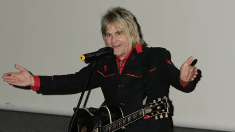 PA Media The Alarm frontman Mike Peters on stage with a guitar around his neck